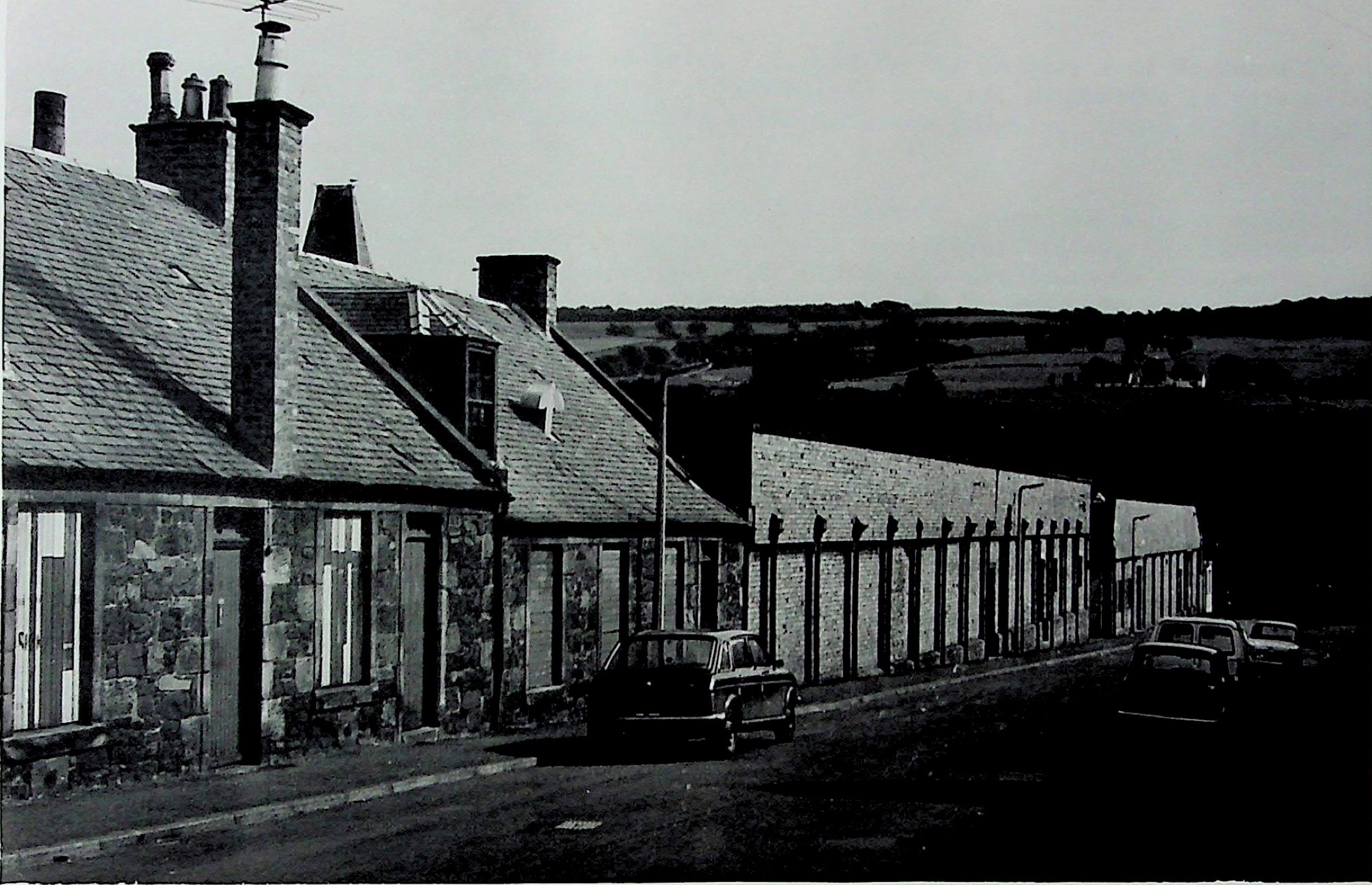 A row of old stone cottages directly beside a long factory wall