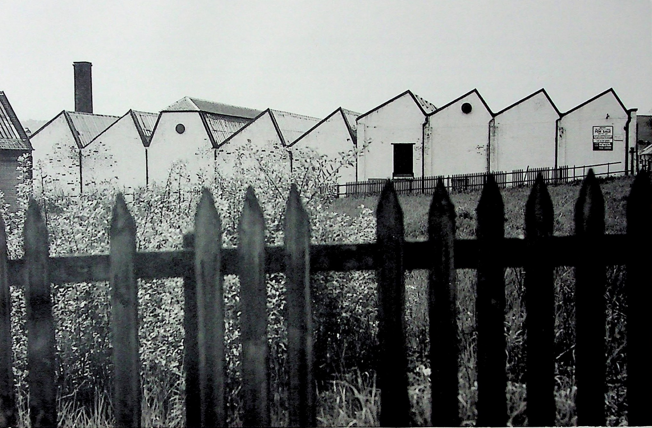 Saw-tooth roofs of a Darvel weaving factory seen behind a fence