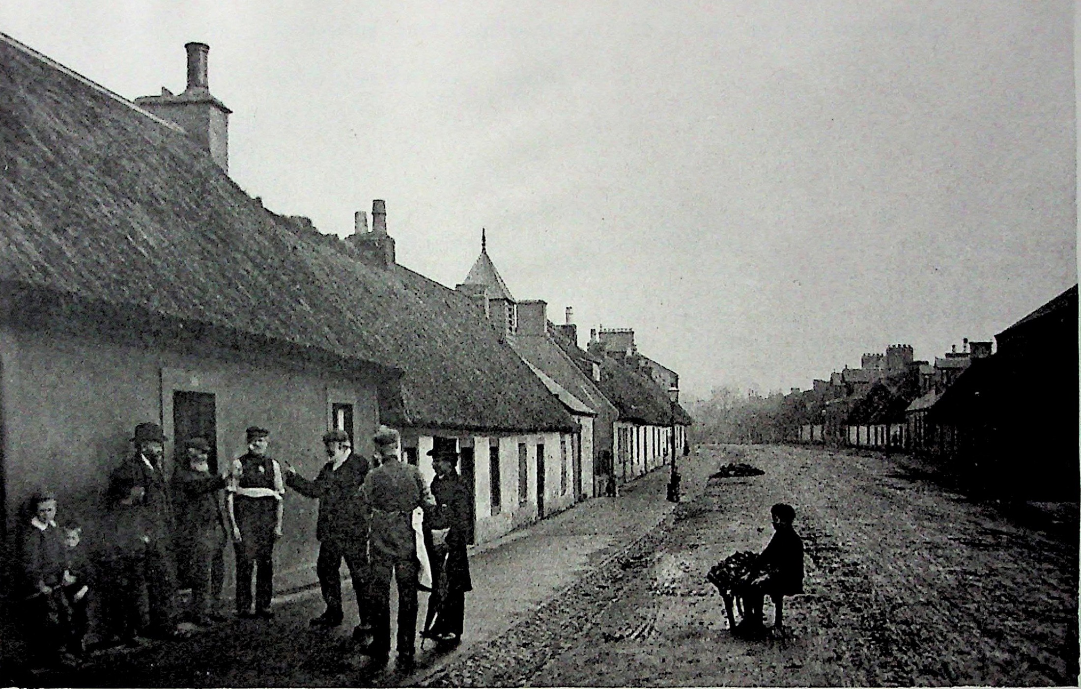 Families standing outside a long row of low weavers’ cottages