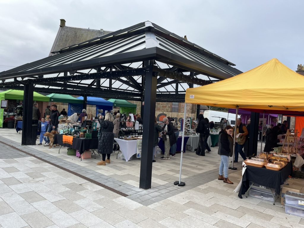 Market stalls and visitors beneath the canopy at The Corner