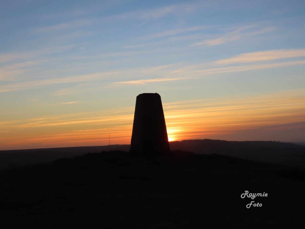 The summit trig point silhouetted against a sunset sky